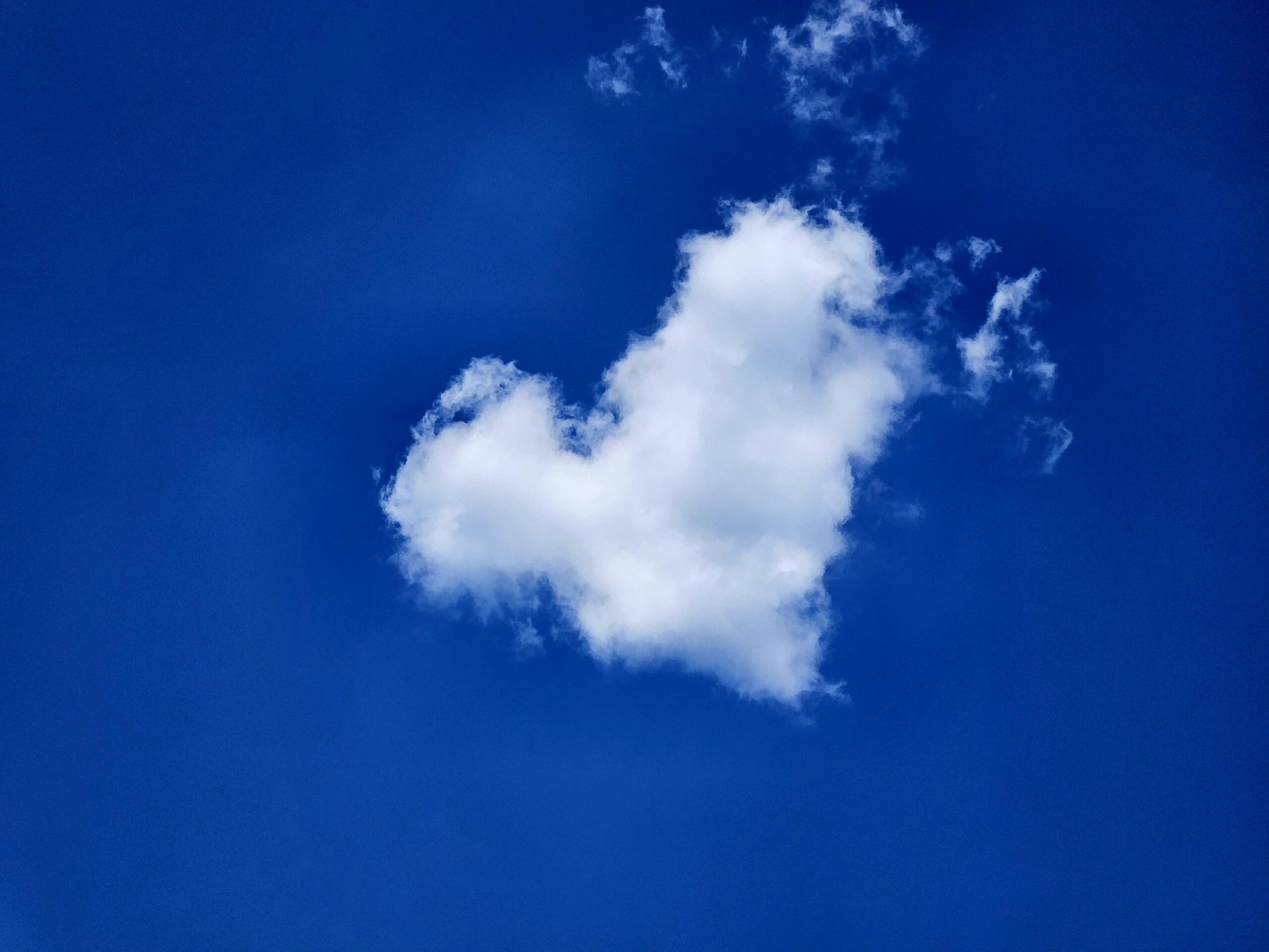 Naturally formed heart-shaped cloud against a clear blue sky.